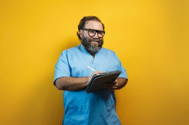 Sarı arkaplanda tablet kullanan mavi ceketli bir doktor. Hastanede teknoloji kullanımı kavramı.