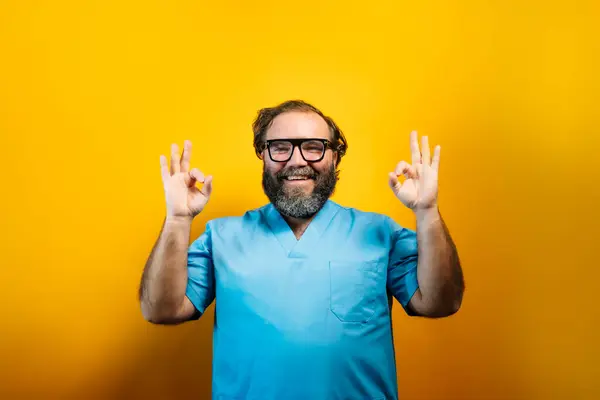 stock image Doctor in blue coat on yellow background gesturing, with OK expression.