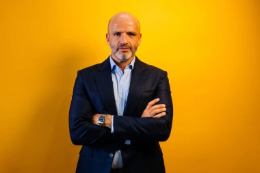 Koyu mavi takım elbiseli bir adam sarı duvarın önünde duruyor..