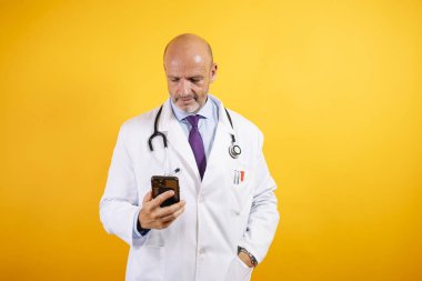 Beyaz önlüklü, dost canlısı bir doktor elinde akıllı bir telefon tutuyor. Modern sağlık ve iletişimi öneriyor..