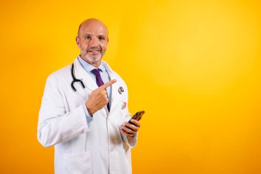 Beyaz önlüklü, dost canlısı bir doktor elinde akıllı bir telefon tutuyor. Modern sağlık ve iletişimi öneriyor..