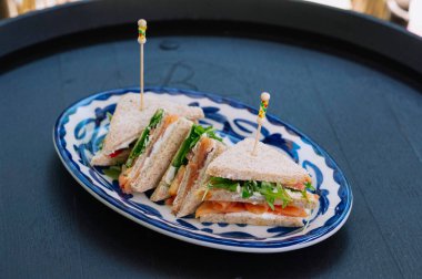 Üç lezzetli füme somon sandviçi ustalıkla bir tabakta servis edilir..