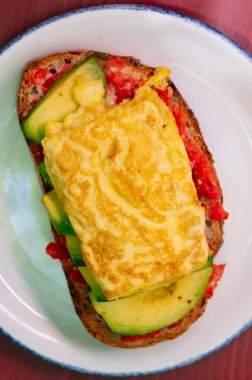 Omlet, avokado dilimleri ve kızarmış domatesli sağlıklı bir açık yüzlü sandviç..