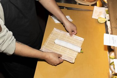 Bir şefin ellerini dikkatlice bambudan bir hasırın üzerinde suşi rulosuna sarın.