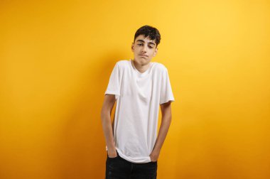 Beyaz tişörtlü, sarı arka planda gülümseyen genç çocuk..