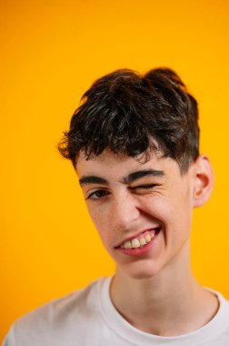 Genç çocuk şakacı bir şekilde sarı arka plana göz kırpıyor.