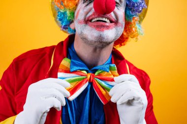 Mutlu palyaço gökkuşağı papyonunu ayarlar, parlak sarı arka plan.