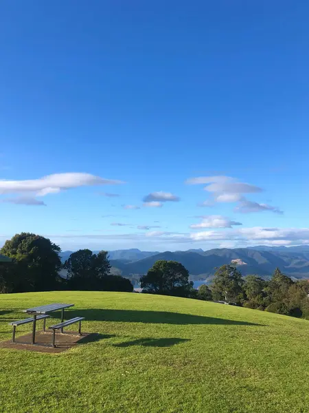 Çimenli bir tepenin üzerinde bir piknik masası, yemyeşil tepeler ve parlak mavi bir gökyüzü içeren huzurlu bir manzara. Doğa, açık hava ya da seyahatle ilgili konular için ideal