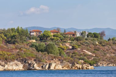 Sithonia yarımadasının arka planında ağaçlar, çalılar ve mavi gökyüzünün olduğu güzel bir deniz manzarası - Chalkidiki - Yunanistan