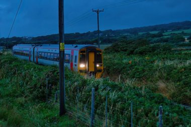 the train is going on the railway at night. in Tal-y-bont - Gwynedd - Wales - Great Britain clipart