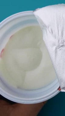 Adam yoğurdu plastik bardakta açıyor. Yeşil arka planda kaşık. Yoğurt probiyotikler, kalsiyum ve proteinle sağlıklı bir atıştırmalıktır. Yerken yemek çok kolay. Sade mi yoksa meyveli ve tahıllı mı?