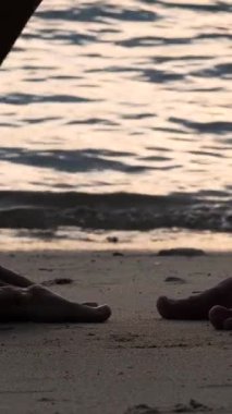 Kumlu sahil şeridinde bacak silueti. Tatlı kız arkadaş ve erkek arkadaş sahilde günbatımının tadını çıkarın. Sevgi dolu çift romantik bir anı paylaşır, balayı için mükemmeldir. Gün batımı deneyimlerini güçlendirir