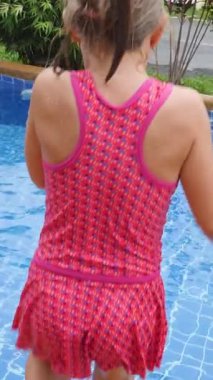 Aktif küçük kız havuzda zıplıyor ve yüzüyor. Tatil köyünde eğlenmeyi seviyor. Yaz tatilinde su sıçrar, dinlenir ve oyun oynar.