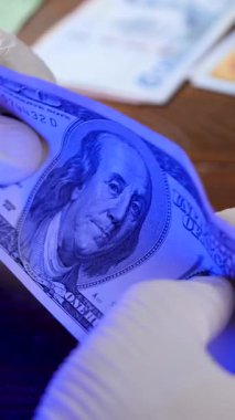 Sahte para için banknot teftişi. 100 Amerikan doları ya da 100 dolarlık banknot. Orijinallik için para ya da nakit geliri değerlendirildi. Doğrulama için ultraviyole ışık altında inceler
