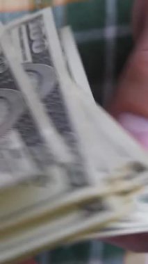 Erkek eller yeşil gömlek arka planında 100 Amerikan doları ya da 100 dolarlık banknot sayıyor. İş ya da mali konsept
