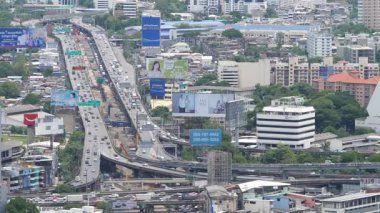 Traffic flows raised highway road, residential and commercial areas. Vehicles navigate urban setting. Tall buildings, green spaces. Top view capital Asia city - BANGKOK, THAILAND - 29 JULY, 2020