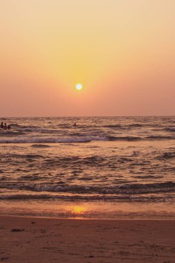Gün batımında sahil, kıyıya yakın köpüğe dönüşen küçük dalgalarla biraz dalgalı bir denizdir. Her şey sıcak kırmızı, pembe, sarı, turuncu renklerle aydınlanır ve ufuktaki sıcak altın güneş mükemmel bir daire şeklinde parlar..