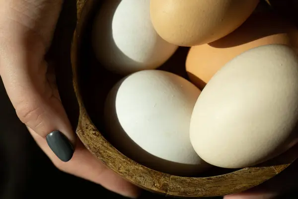 Natural, organic farm product in the form of chicken eggs with shells of different colors. Female hands hold a wooden plate with chicken eggs.