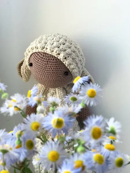 A knitted toy in the form of a sheep with small blue wildflowers. Portrait photo of a toy on a white background.
