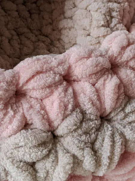 Knitted product from soft plush yarn with a clear pattern in pleasant pastel colors. Texture of a knitted blanket.