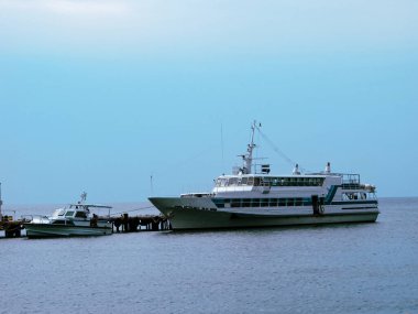İki gemi küçük bir hangara demirlemiş. Etrafında pürüzsüz mavi deniz suyu ve açık mavi güneşli bir gökyüzü var..