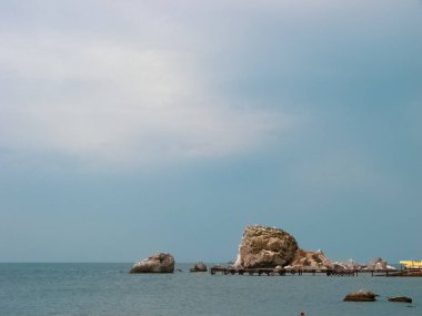 Sakin deniz suyunun arasında, berrak mavi ılık yaz gökyüzünün arka planında, küçük taş kayalar var..