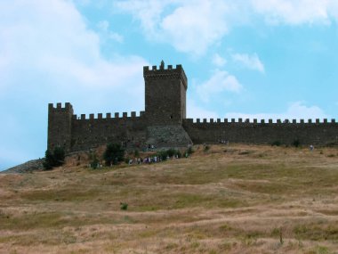 Açık mavi bir gökyüzünün arka planında, taştan bir kayanın üzerindeki ortaçağ kalesi.