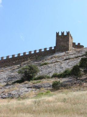 Açık mavi bir gökyüzünün arka planında, taştan bir kayanın üzerindeki ortaçağ kalesi.