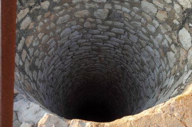 Derin, tarihi bir taş kuyusu, karanlık bir iç mekanı, kırsal bir alanda antik taş işçiliği sergiliyor..