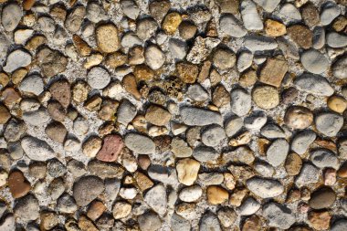 Betona gömülü küçük, pürüzsüz taşlardan oluşan bir çeşitliliğin sergilendiği desenli çakıl taşı kaldırımının yakın çekim görüntüsü..