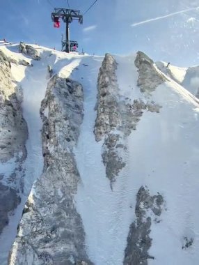 Bir teleferik, açık mavi gökyüzünün altında kar kaplı dağların üzerinde süzülüyor..