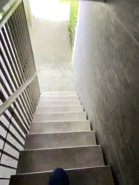 Beton duvarlar ve metal korkuluklar ile çerçevelenmiş asfalt bir avluya giden merdivenin tepesinden manzara.