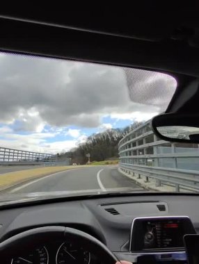 Çarpıcı, bulutlu gökyüzünün altında kavisli bir köprüde giden bir arabanın içinden görüntüyü izleyeceğiz..