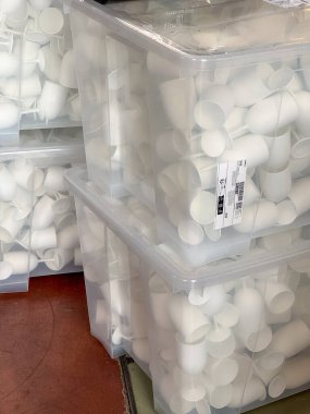 Geniş saydam plastik kutular istiflenmiş ve sayısız küçük plastik bardaklarla doldurulmuş, depolama, paketleme ve yemek malzemelerini sembolize ediyor..