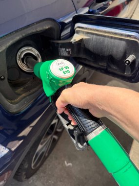 Yakından, yakıt, enerji ve ulaşımı sembolize eden yeşil benzin pompalı bir arabaya yakıt ikmali yapan bir kişi..