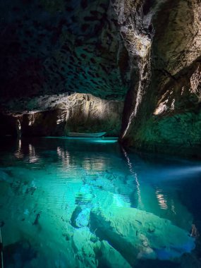 Işık yansımalarının gizemli ve büyüleyici bir atmosfer yarattığı engin bir yeraltı mağarasının kemerli tavanının altında parlayan turkuaz bir göl..