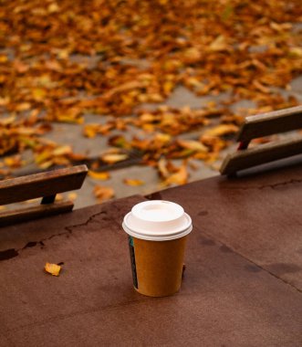 Ahşap bir masanın üzerine düşmüş sarı yapraklardan oluşan bir arka planda bir bardak sıcak kahve. Yüksek kalite fotoğraf