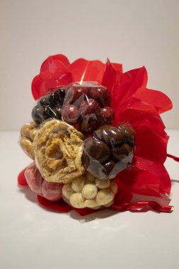Çiçeklere sarılı, kırmızı ambalajlı, beyaz arka planda çikolata kaplı fındık buketi. Yüksek kalite fotoğraf