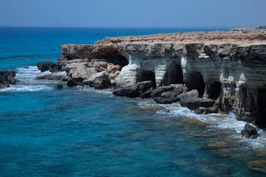 Açık turkuaz deniz, kayalık kıyı şeridi ve Kıbrıs 'taki mağaralar. İnsansız huzurlu bir manzara, seyahat ve doğa kavramları için ideal..