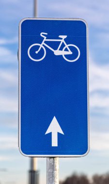 Şehir ortamlarında bisiklet altyapısının altını çizerek, temiz bir gökyüzüne karşı yönlü bir okla mavi bisiklet şeridi tabelasına yakın çekim.