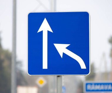 Önünde beyaz oklar ya da sağa dönüş işareti olan mavi bir yol işareti. Bulanık şehir arkaplanı.