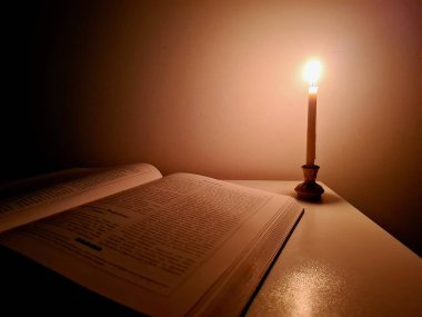 Açık bir kitap ve mum ışığında yanan bir mumla atmosferik bir sahne yayılmış sıcak bir ışık yaratıyor. Kitabın sayfaları, resme sakinlik, yalnızlık ve konsantrasyon hissi veren yumuşak bir alevle aydınlatılıyor. Konular için mükemmel