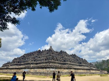 A view of the Borobudur Temple in Indonesia, a massive Buddhist monument with intricate carvings and a tiered structure, set against a blue sky with white clouds.  clipart