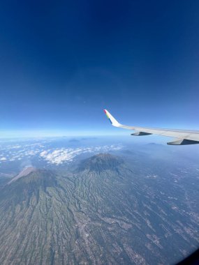 Volkanların ve bulutların uçak kanadı görüntüsü. Orta Cava 'daki Merapi Dağı ve Merbabu Dağı manzarası