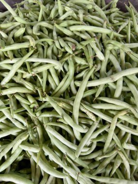 Bir sepet ya da konteynırda üst üste yığılmış taze taze toplanmış taze fasulyelerin yakın çekim görüntüsü. Fasulyeler açık yeşil ve yerel bir markette satılmaya hazır görünüyor..