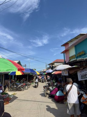 Güneydoğu Asya 'da açık mavi gökyüzünün altında renkli şemsiyeler, satıcılar ve müşterilerle dolu hareketli bir sokak pazarı var..
