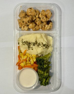 Sağlıklı bir yemek kabı ızgara tavuk, kremalı patates püresi, karışık sebze havucu, mısır, brokoli ve yanında sos..