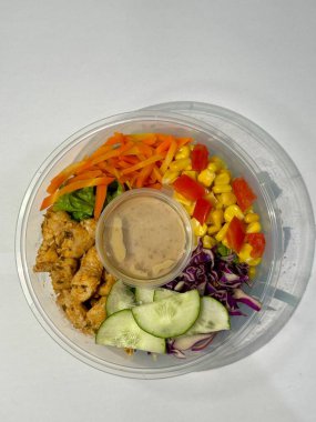Canlı bir tavuk salatası kasesinde ızgara tavuk, doğranmış havuç, mısır, salatalık, kırmızı lahana ve kremalı sos yer alır. Plastik bir kapta sunuluyor..