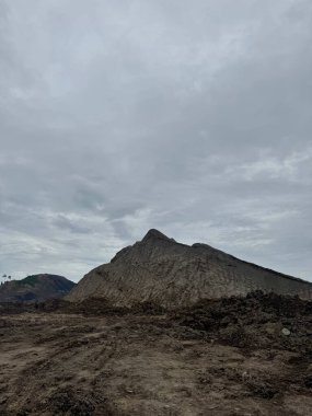 Gri gökyüzünün altında büyük bir dağı gösteren çarpıcı bir manzara. Sahne, huşu ve doğanın gücünü çağrıştırıyor..