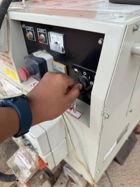 Bir işçi eli, endüstriyel güç ekipmanları ve elektrik bileşenlerini detaylı bir yakın çekim görüntüsünde gösteren bir jeneratör kontrol panelini çalıştırır..